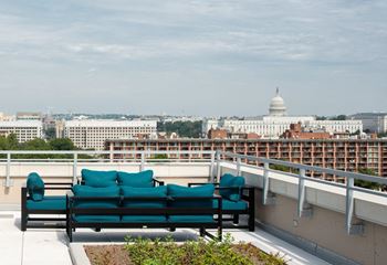 A bench with green cushions is on a balcony overlooking a cityscape.